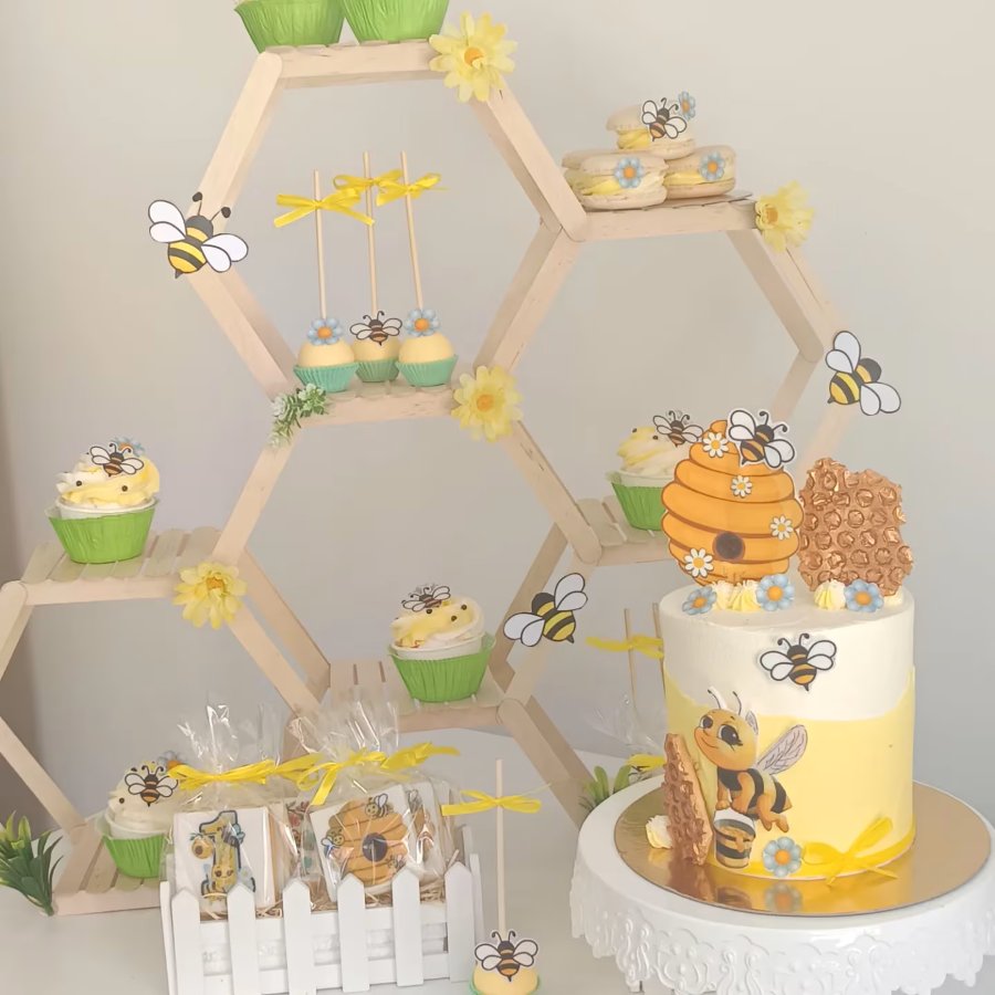 Taula dolça amb temàtica d'abelles: pastís i cupcakes en un expositor de bresca